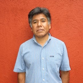 Fulgencio Lazo pictured in a light blue checkered button-up shirt in front of an orange background